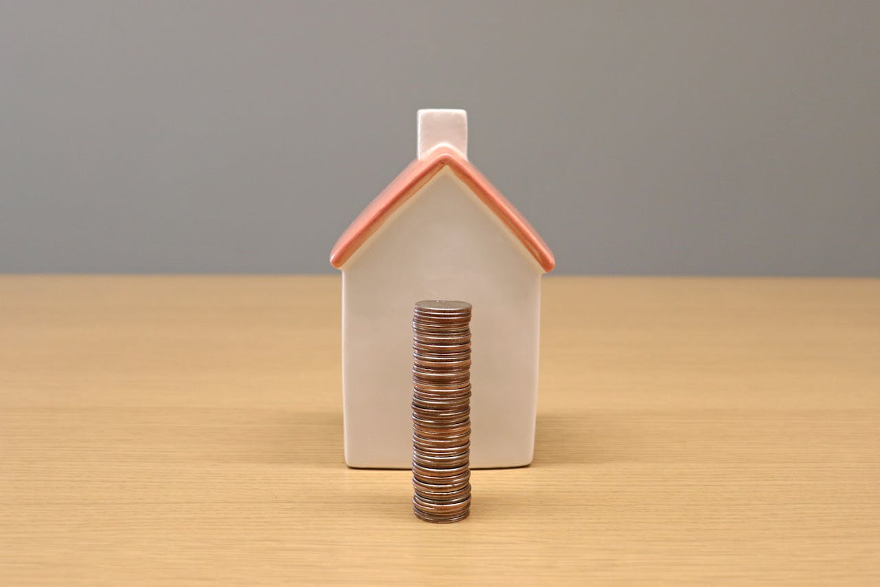 A conceptual still life image of stacked coins in front of a porcelain house, symbolizing savings and investment.